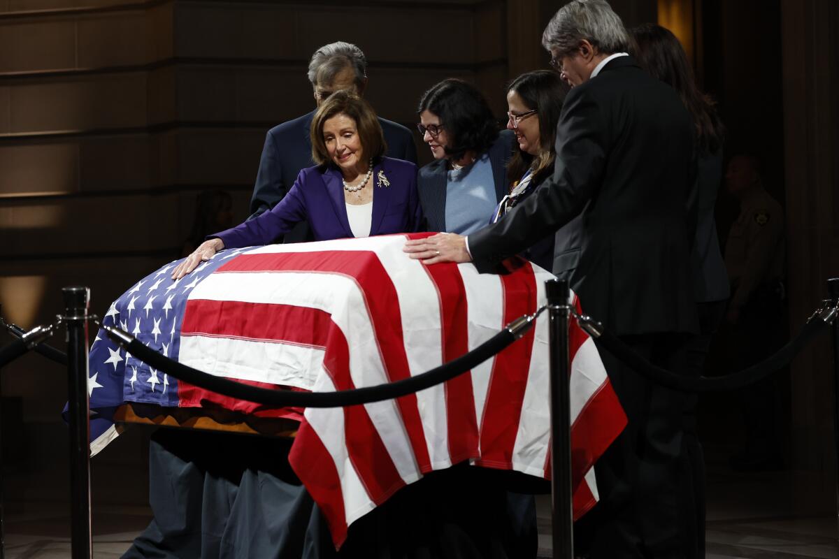 A woman and a man each place a hand on a flag-draped casket as other people look on 