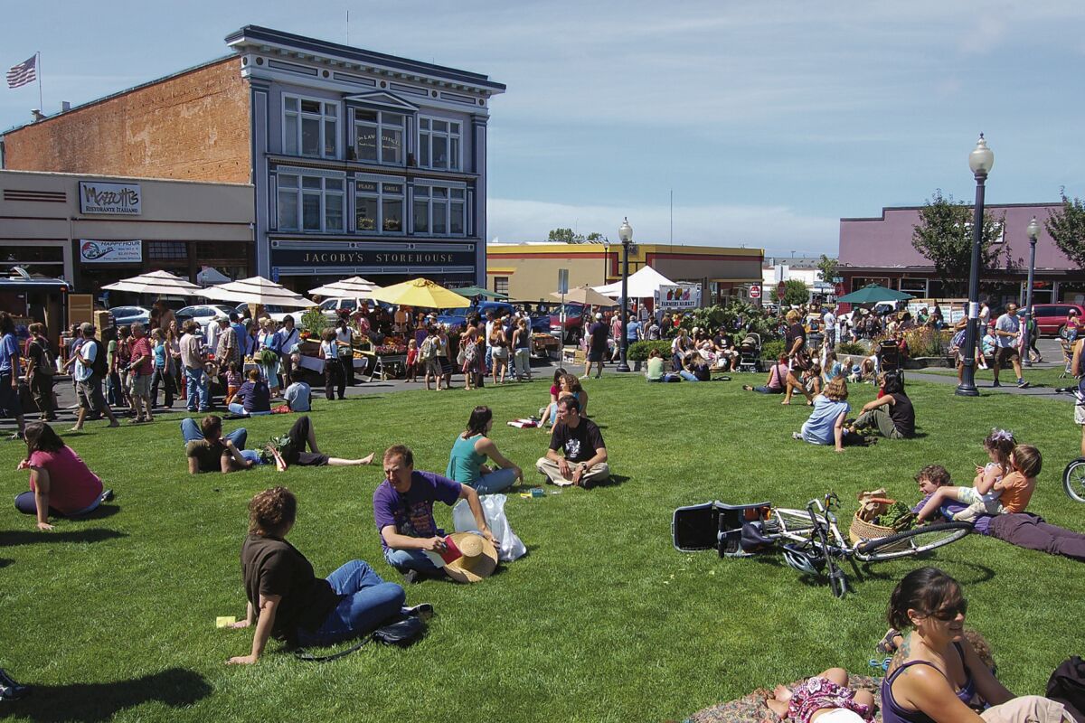 People sitting on the ground in a grassy plaza, with old brick buildings behind.