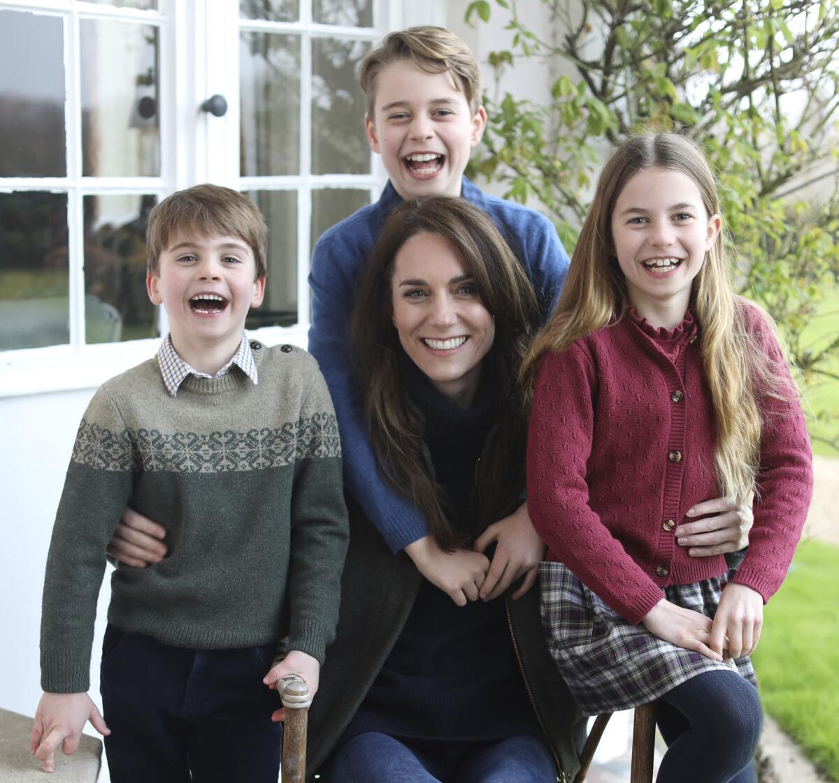 A woman, seated, flanked by the three grinning youngsters in cozy sweaters