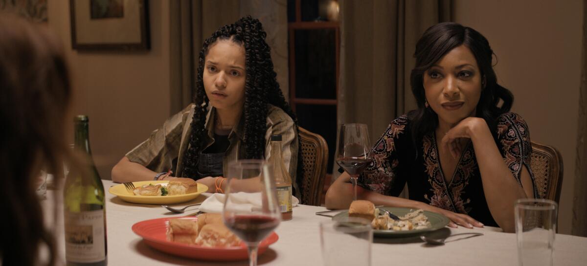 A teenage girl and her mother sit side by side at the dinner table.