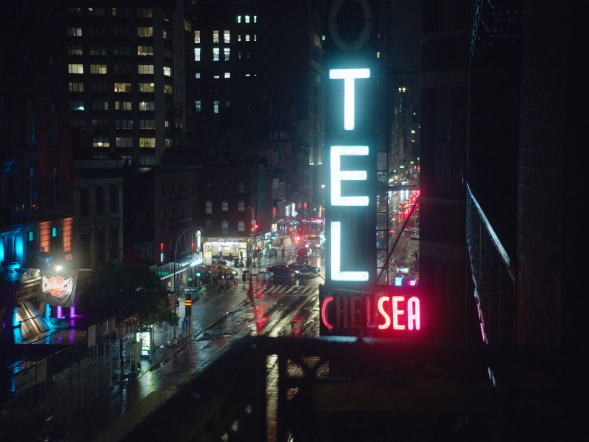 The neon sign of the Chelsea Hotel at night above a wet street in the documentary "Dreaming Walls: Inside the Chelsea Hotel."