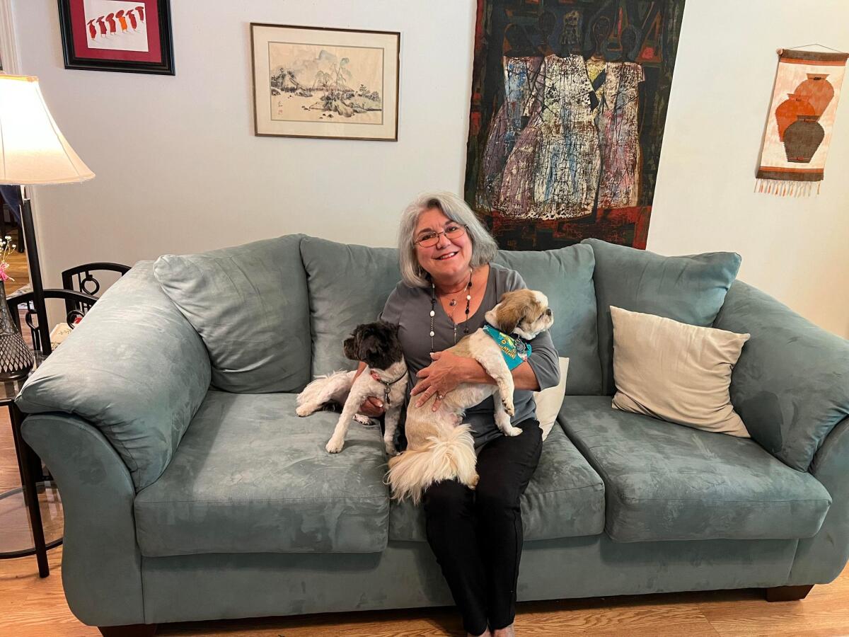 A woman holds two dogs while sitting on a couch