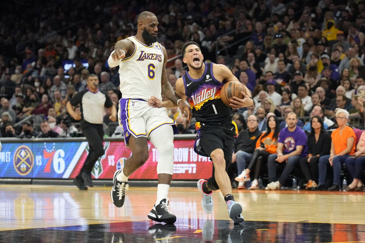Phoenix Suns guard Devin Booker (1) is pressured by Los Angeles Lakers forward LeBron James during the second half of an NBA basketball game, Sunday, March 13, 2022, in Phoenix. (AP Photo/Rick Scuteri)