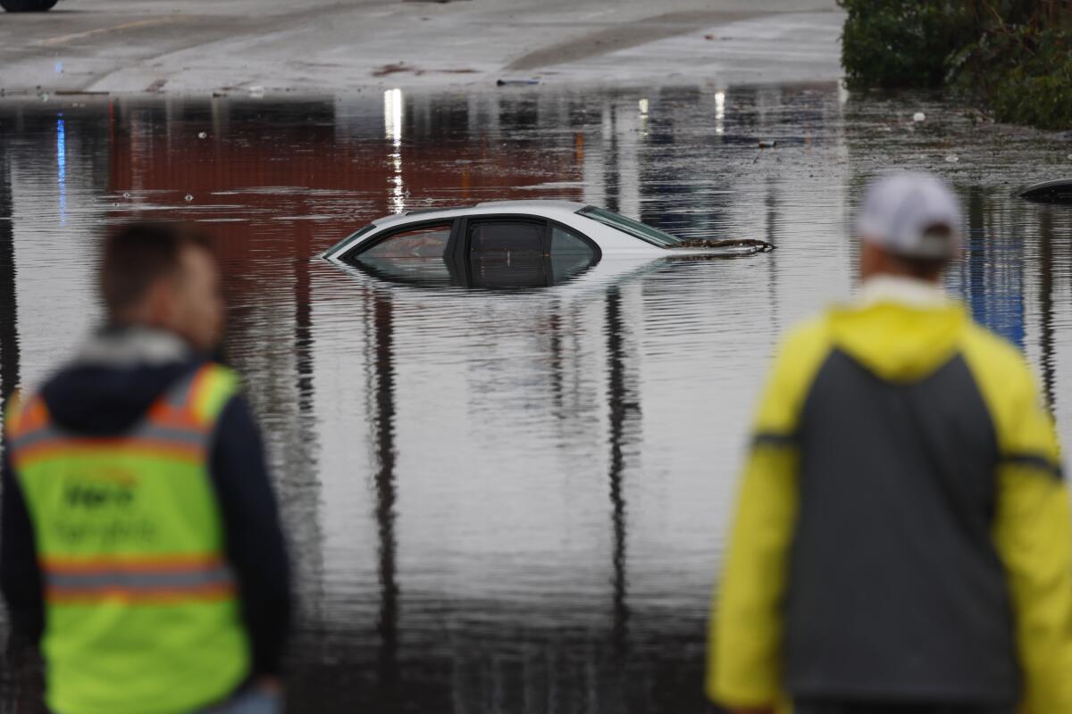 A car is submerged in water as two people watch.