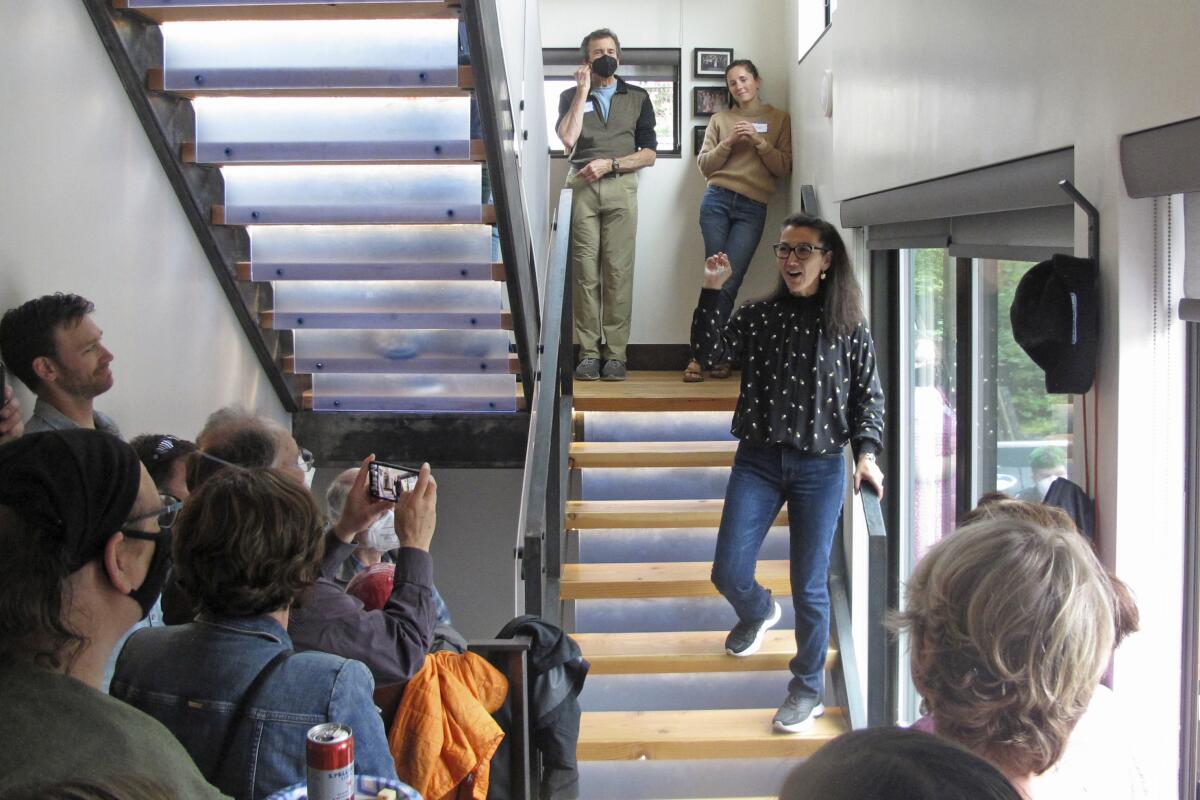 A woman in jeans standing on a staircase, speaking to a small group below her. 