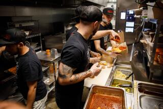 Calvin Skarlat, center, front, passes a seasoned piece of hot fried chicken to Ethan Valenzuela and Kevin Popok, far right, as they prepare Nashville style hot fried chicken sandwiches and fries in the Main Chick Hot Chicken kitchen at Colony on Saturday, January 18, 2020 in Los Angeles, Calif. Colony offers 26 kitchen spaces for rent by restaurants - sometimes referred to as "ghost kitchens" or "virtual kitchens" - where restaurants prepare meals for delivery or pickup to serve consumers using Grubhub, Uber Eats, DoorDash, and other online-based services. (Patrick T. Fallon/ For The Los Angeles Times)