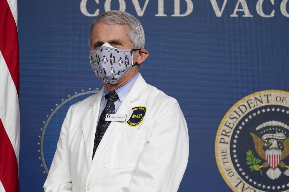 A closeup of Anthony Fauci, double masked and wearing his white NIAID coat.