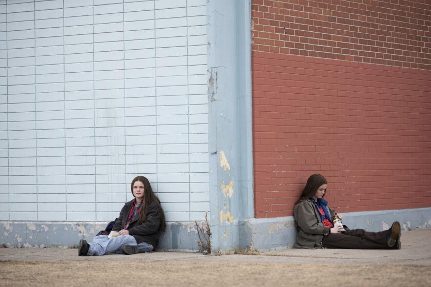 Two teenage girls sitting on the ground by the corner of a building