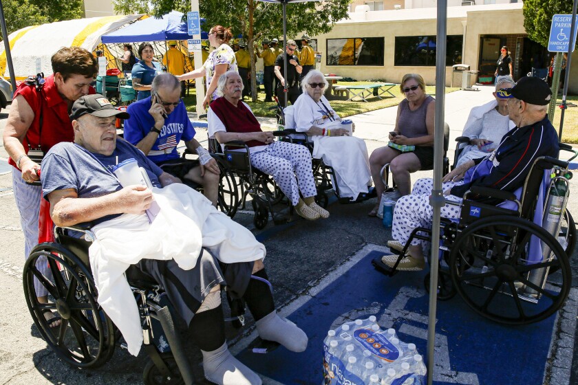 Patients sit in wheelchairs under an outdoor shelter.