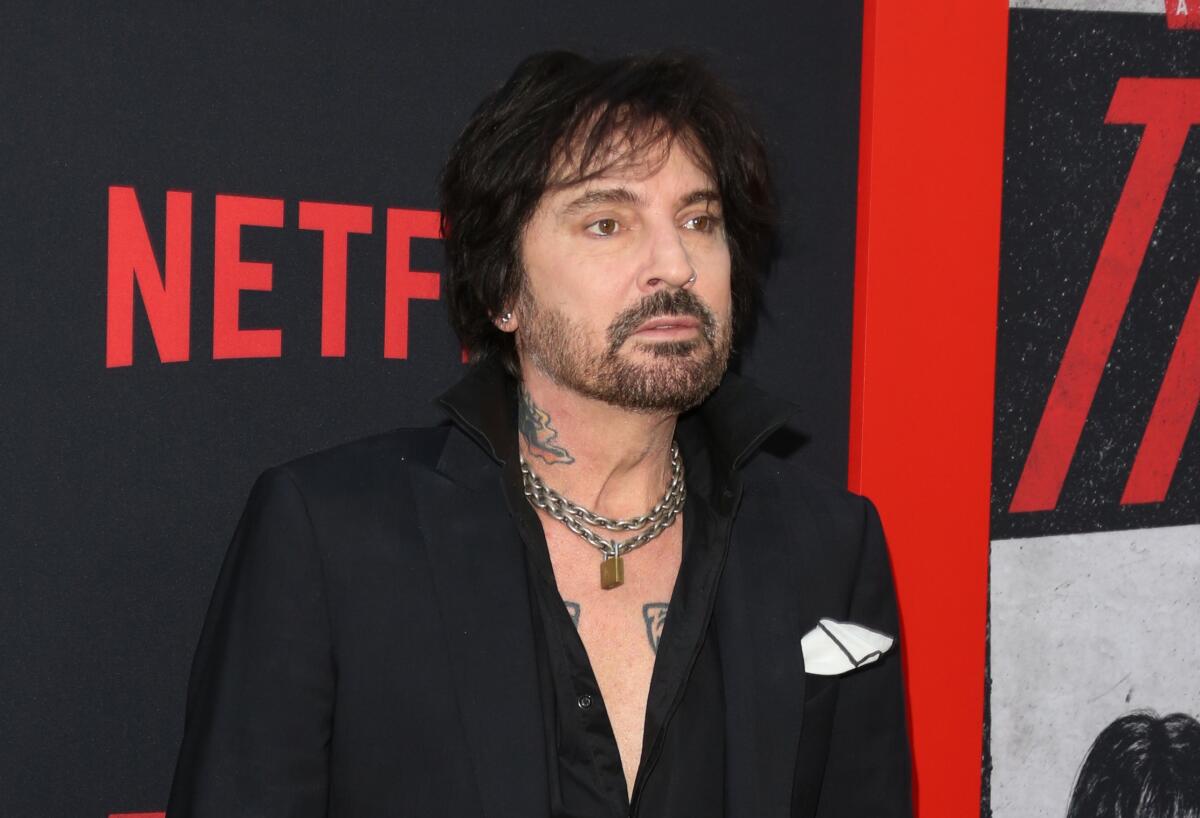 Tommy Lee stands in front of the Netflix logo on a red carpet.
