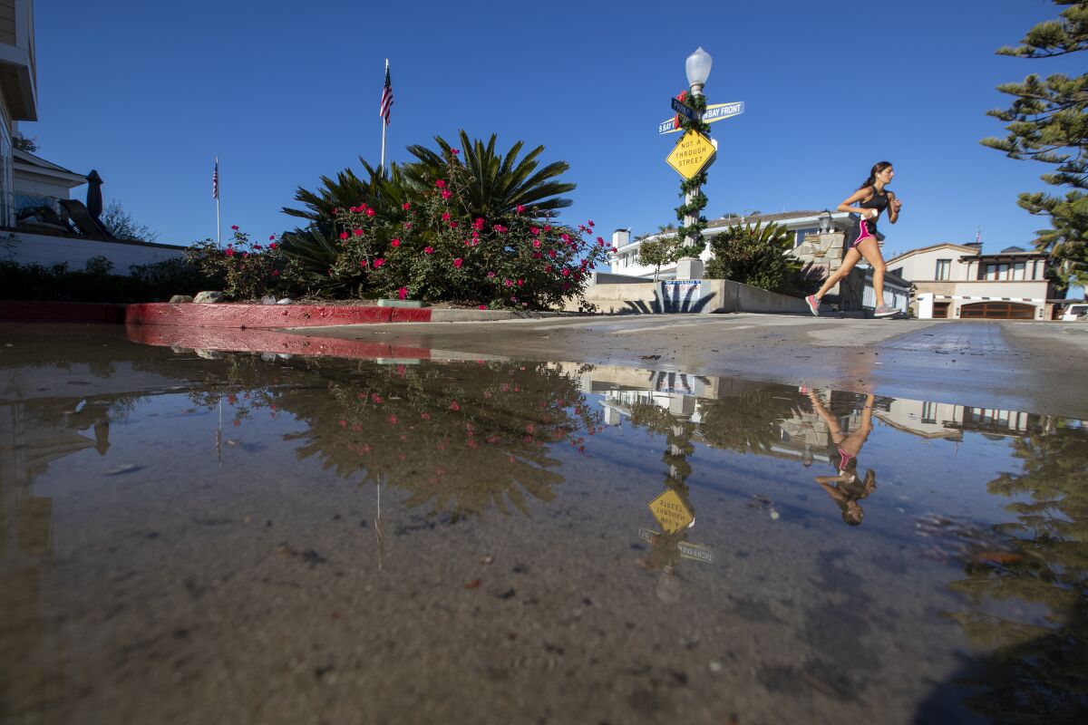 A jogger is reflected in minor street flooding following king tides on Balboa Island in Newport Beach.
