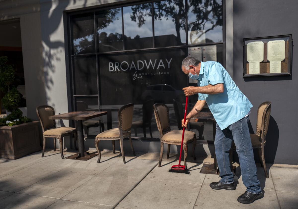 A man wears a mask while sweeping outside a restaurant in Laguna Beach.