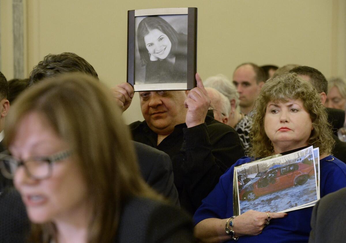 Leo Ruddy, back left, and Mary Theresa Ruddy of Scranton, Pa., hold up pictures of their 21-one-year-old daughter Kelly and the 2005 Chevy Cobalt that she died in in 2010, during testimony from General Motors CEO Mary Barra, front left, at the Senate Commerce, Science and Transportation subcommittee hearing Wednesday.