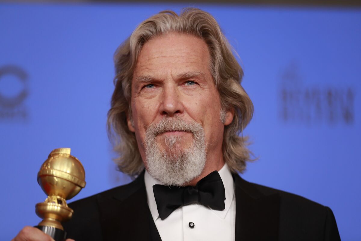 A bearded man in a tux holds a Golden Globe award