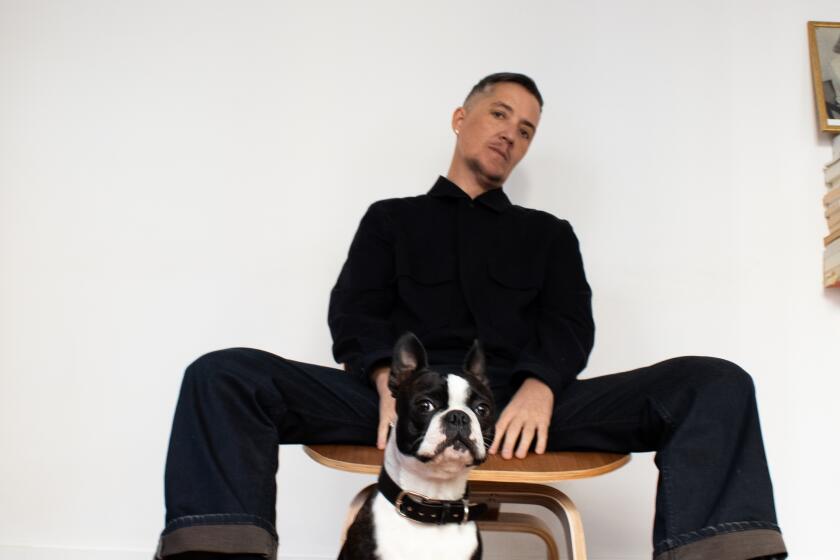 A person sits in his chair, with his Boston terrier in front of him.