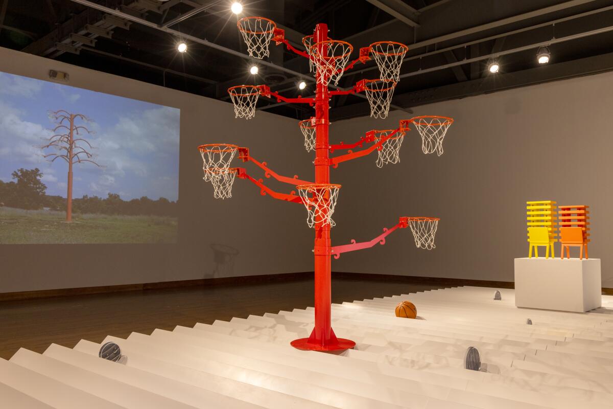 Bright architectonic sculptures, one resembling a tree with basketball nets, rest on a zigzagging white plinth