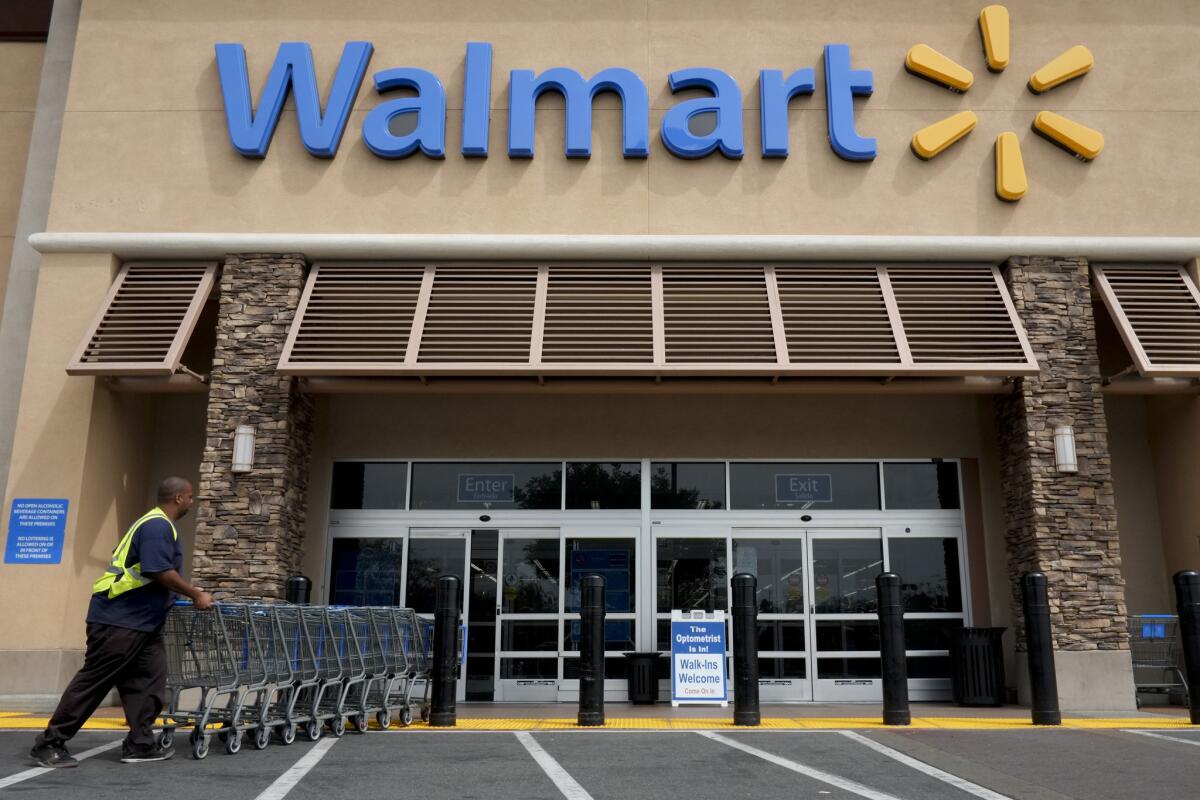 In this May 2013 photo, a worker pushes shopping carts in front of a Walmart store in La Habra, Calif. Wal-Mart Stores Inc. revealed Tuesday that it plans to end health benefits for all part-time workers who average less than 30 hours a week.