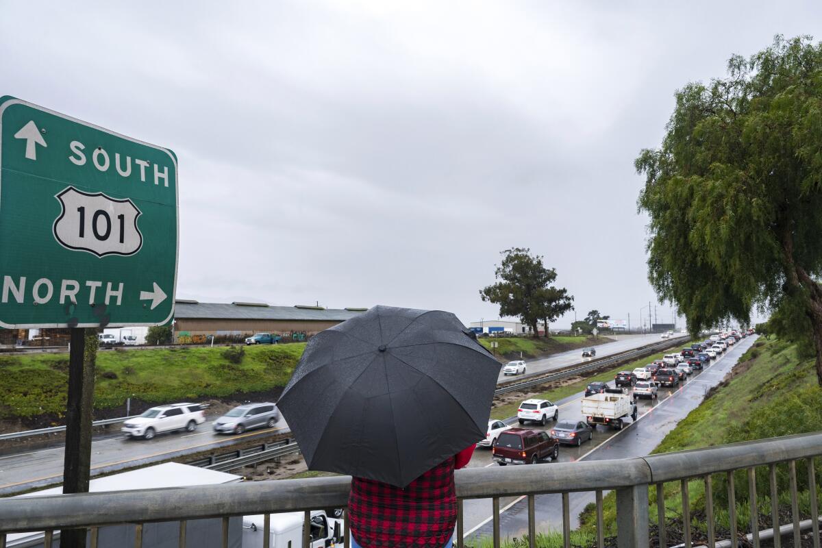 A person holding an umbrella looks out over cars stopped on the 101 Freeway