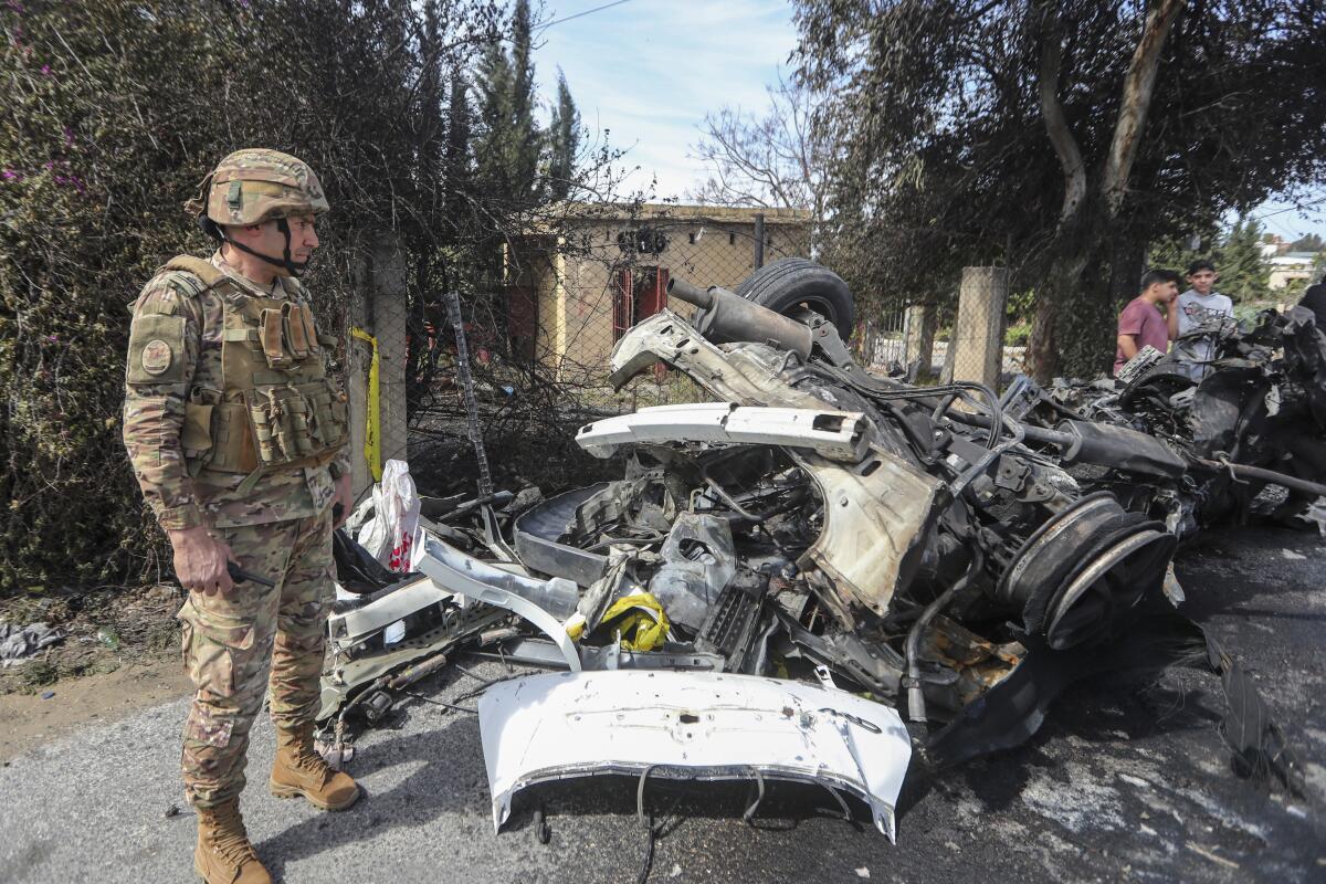A soldier stands next to the remains of a car.