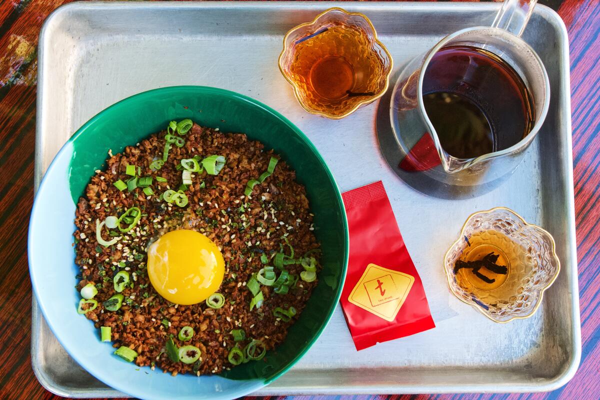 An overhead view of a tray with tea and a smoked chicken rice bowl topped by an egg yolk