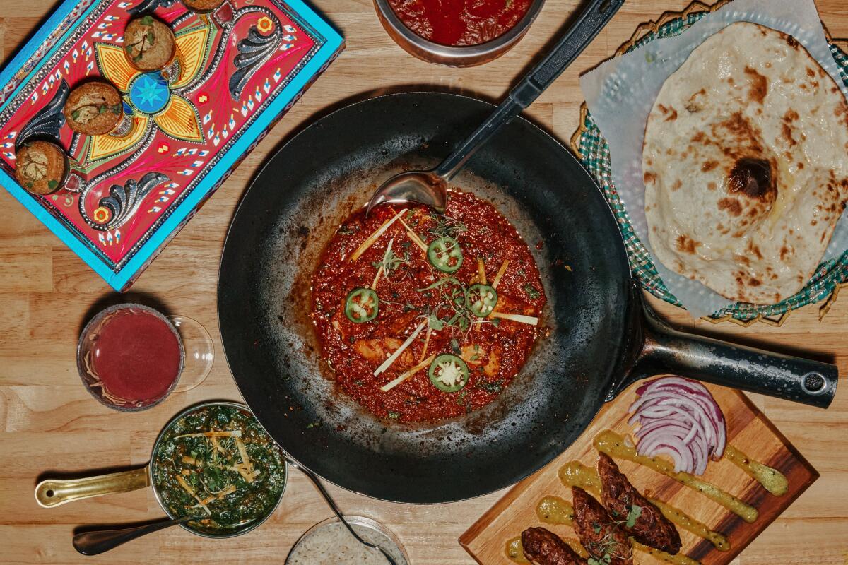 Small dishes surround a large skillet of chicken karahi, with naan on the side, at a restaurant.