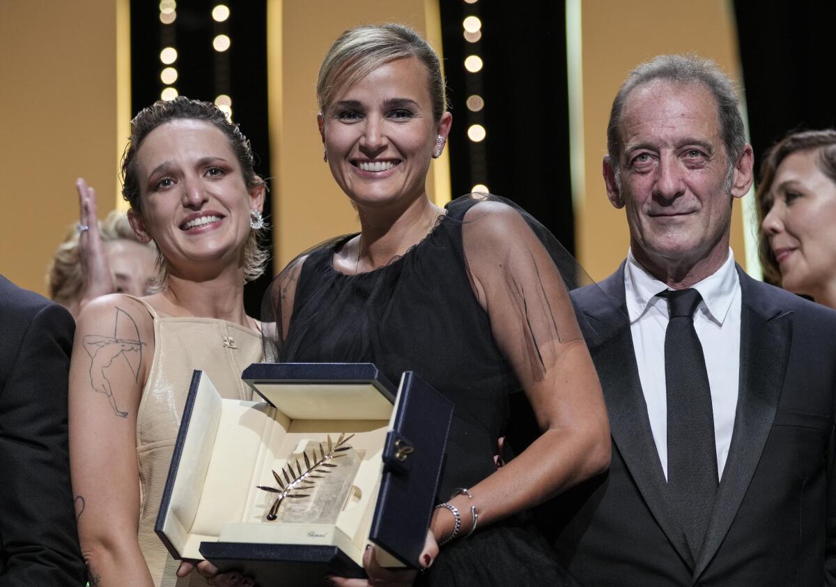 Two women, left, hold an award, and a man stands next to them