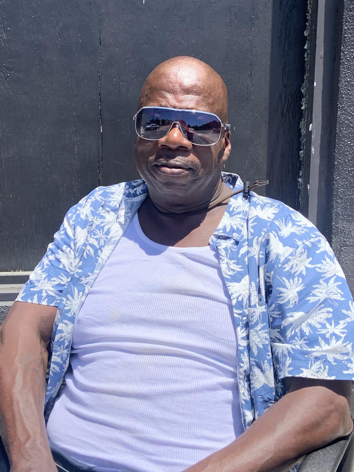 Un homme noir de 55 ans portant des lunettes de soleil assis à l'extérieur