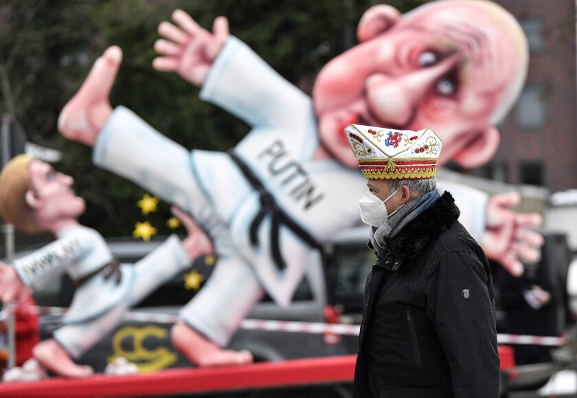 A reveller stands in front of a political carnival float depicting Russia's President Vladimir Putin fighting with opposition leader Alexei Navalny in the streets of Duesseldorf, Germany, Monday, Feb. 15, 2021. Because of the coronavirus pandemic the traditional 'Rosenmontag' carnival parade are canceled but eight floats are pulled through the empty streets in Duesseldorf, where normally hundreds of thousands of people would celebrate the street carnival. (AP Photo/Martin Meissner)