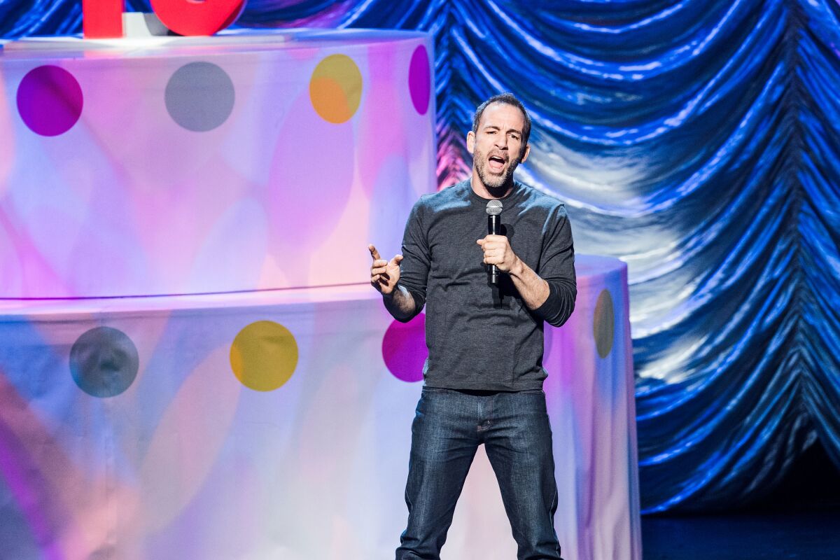 Bryan Callen on a colorful stage set with a microphone, a photo from 2008.