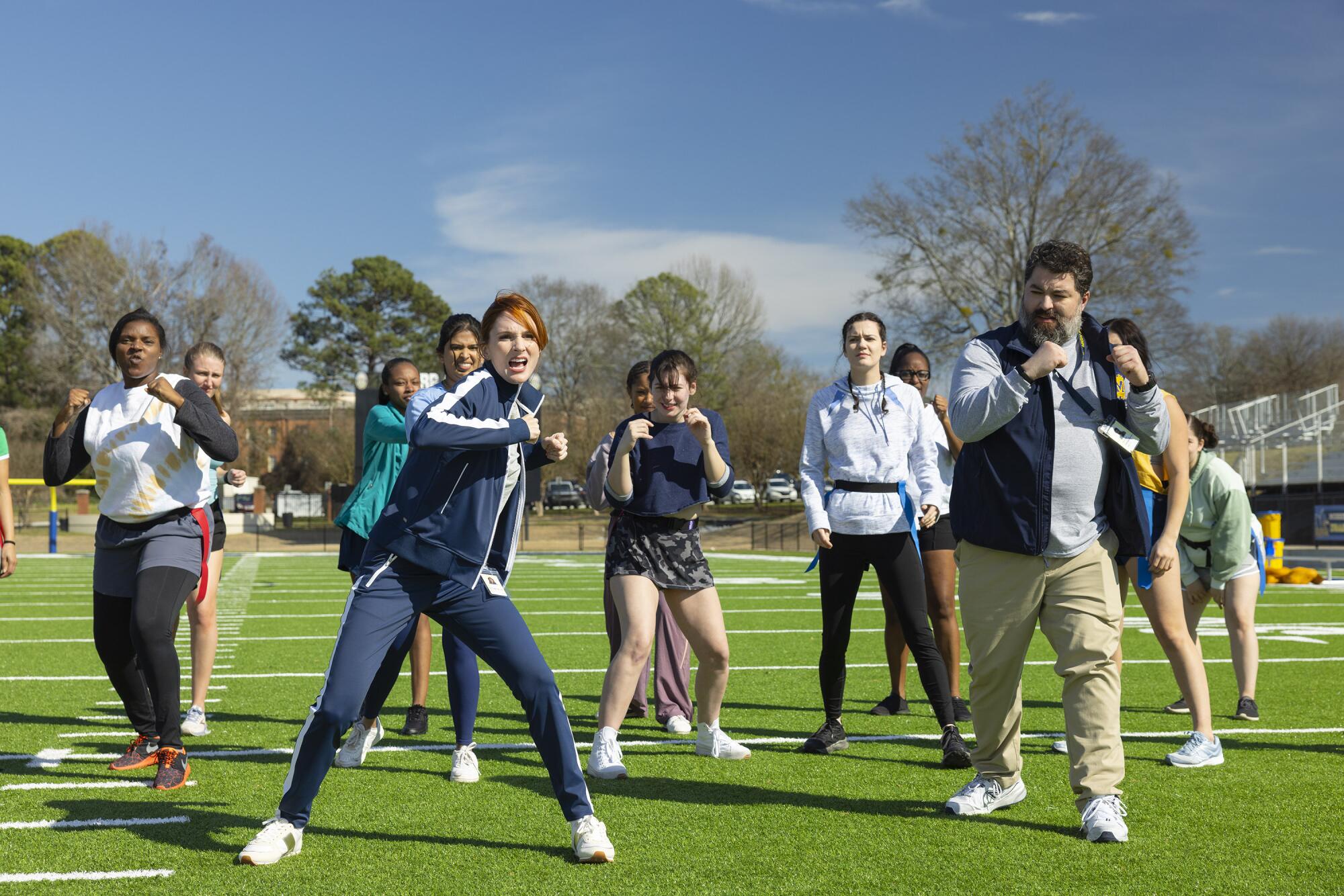 Two coaches standing in front of a group of girls with their fists in the air on a green soccer field.