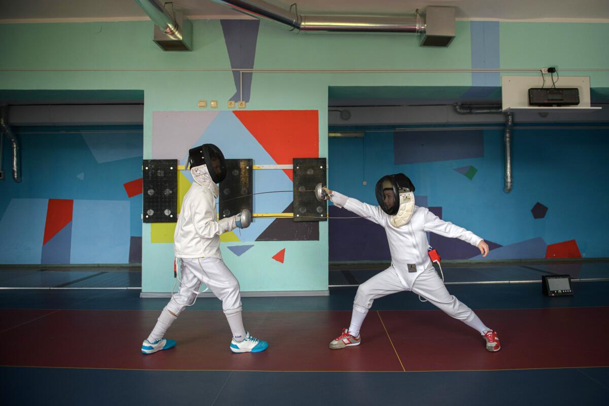 Two children spar, wearing protective helmets. One makes a touch, their weapon flexing as they lunge.