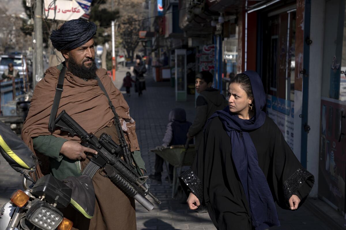 A woman glances at an armed Taliban guard as she walks past him on a city street.