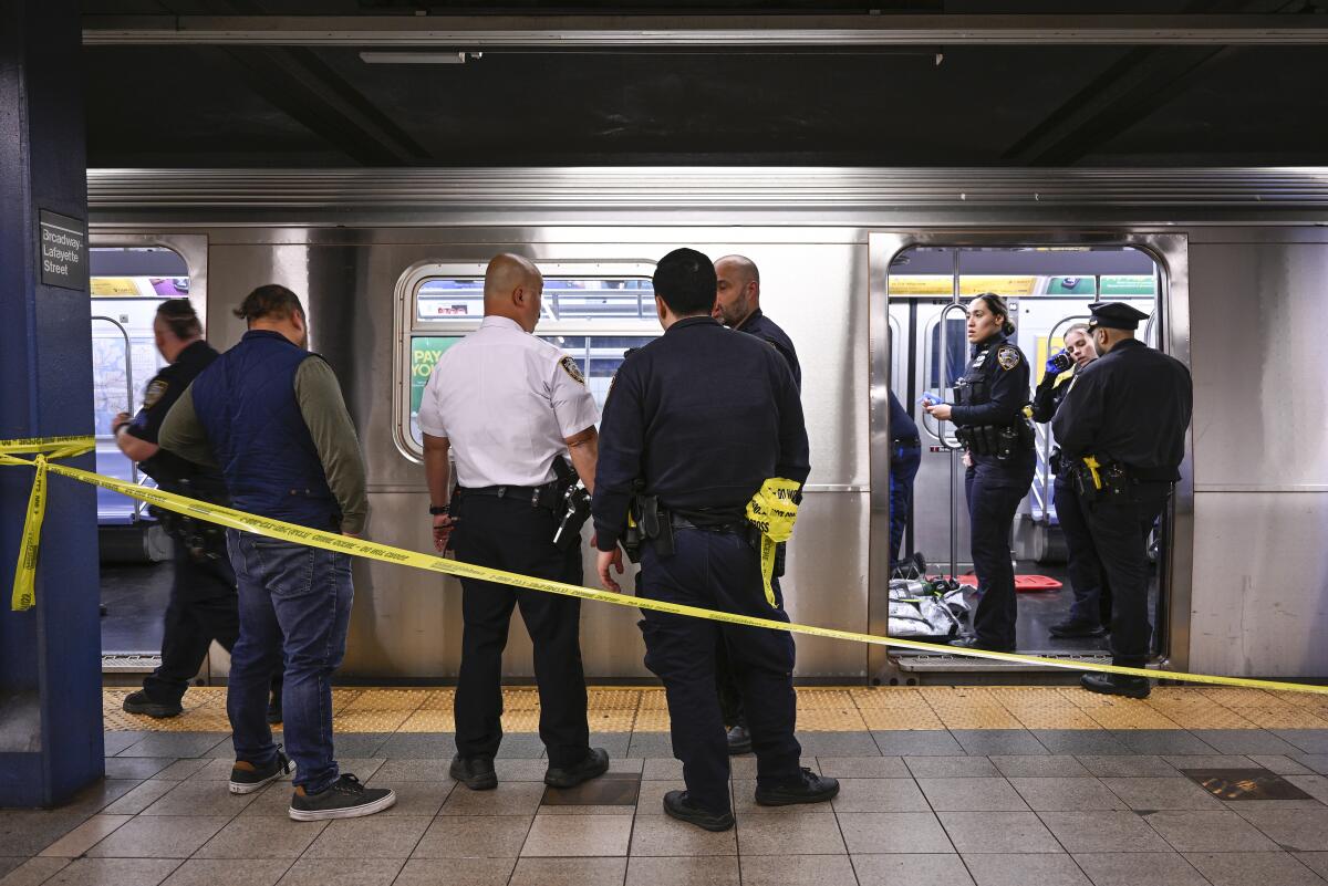 Police officers and others standing in and around a subway car behind yellow crime scene tape