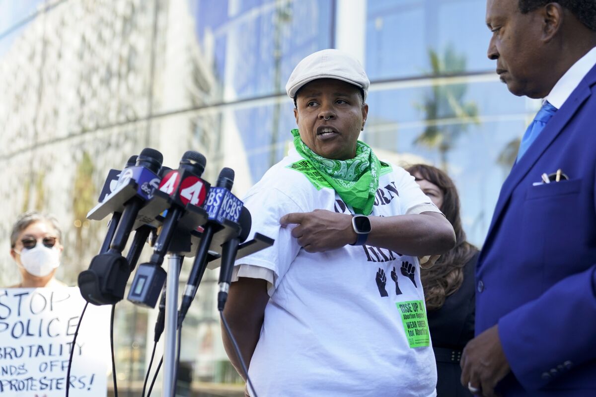 Kareim McKnight, center, talks to reporters during a press conference outside Chase Center, announcing the filing of a federal civil rights lawsuit against the San Francisco Fire and Police Departments in San Francisco, Wednesday, Aug. 10, 2022. McKnight alleges a paramedic, under the orders of a police sergeant, injected her with a sedative while she was handcuffed after protesting the Supreme Court's Roe v. Wade decision during a Golden State Warriors championship game. (AP Photo/Godofredo A. Vásquez)
