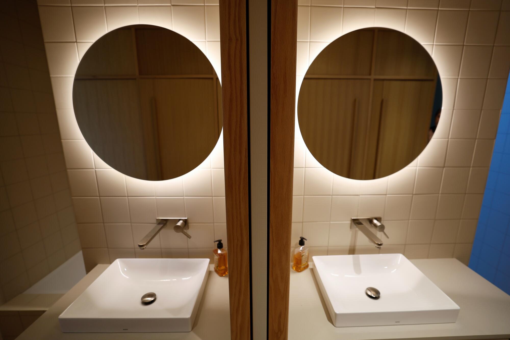 Light glows behind a mirror above a sink, reflected in a mirror. 