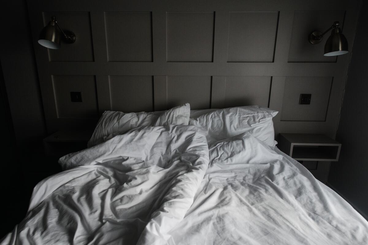 An empty bed with mussed sheets and pillows