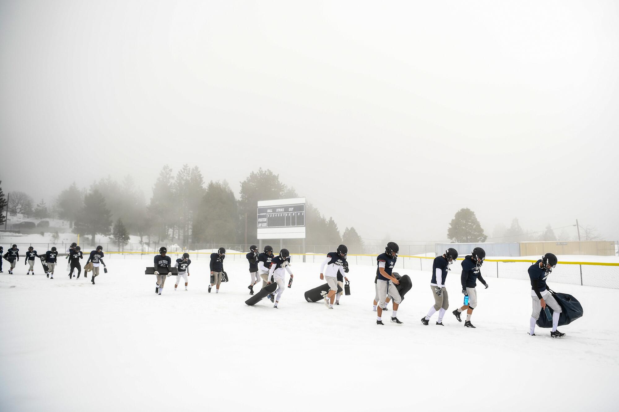 Rim of the World High School football players walk to the practice field after a snowstorm