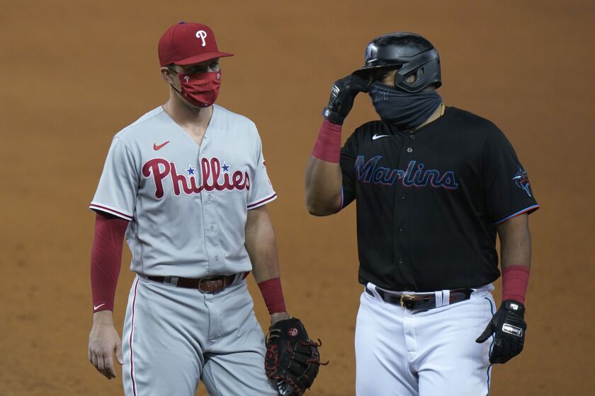 Wearing masks to help prevent the spread of the new coronavirus, Philadelphia Phillies first baseman Rhys Hoskins, left, talks with Miami Marlins' Jesus Aguilar during the fourth inning of a baseball game, Saturday, Sept. 12, 2020, in Miami. (AP Photo/Wilfredo Lee)