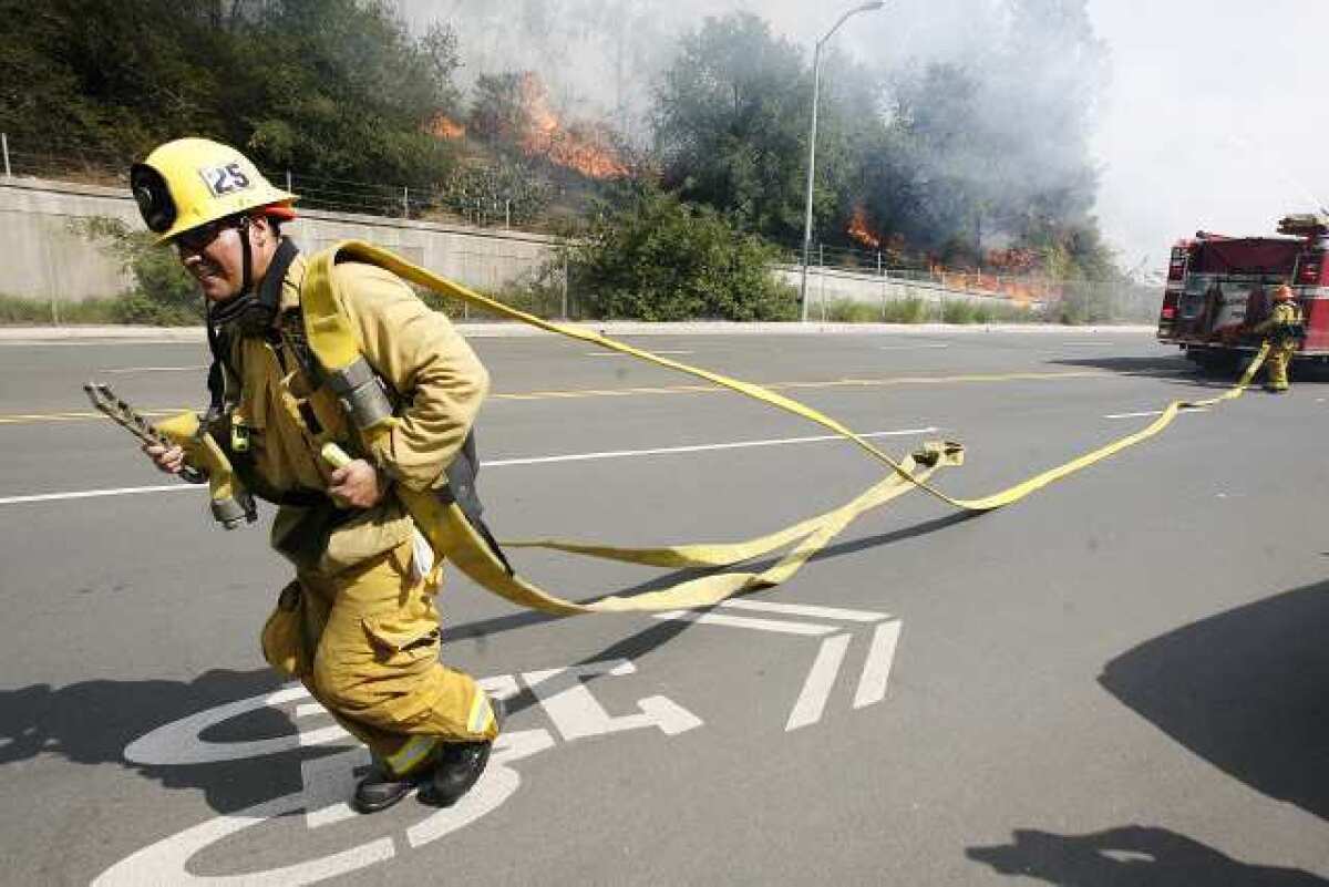 A fireman from Glendale Station 25 runs with hose to connect to a hydrant on Harvey Avenue to battle a brush fire that erupted along the road which was part of a bigger fire in the Glenoaks and Chevy Chase canyons in Glendale on Friday, May 3, 2013. Hundreds of homes were evacuated.