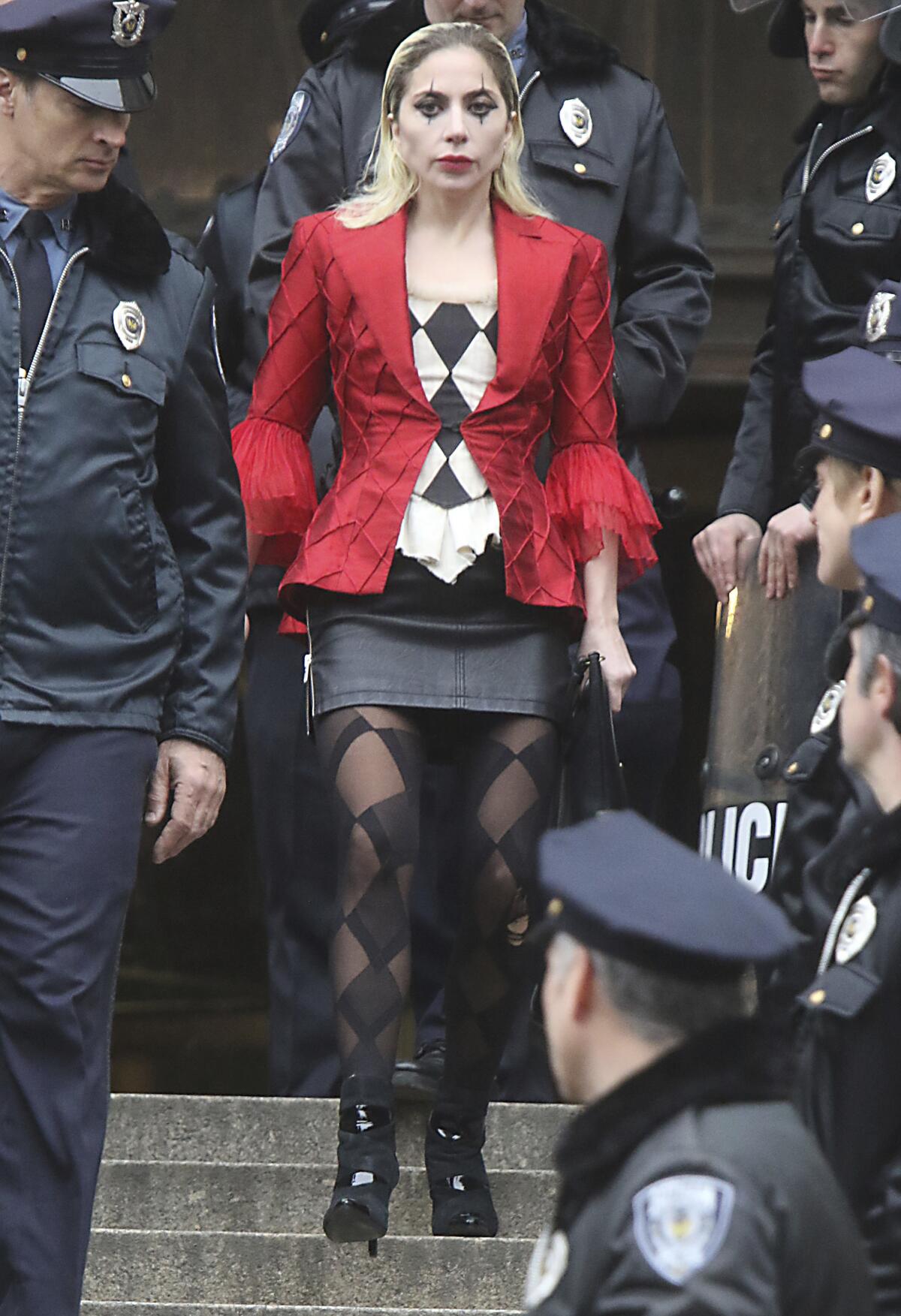 Lady Gaga wearing face paint, a patterned shirt and a red jacket while walking through a crowd