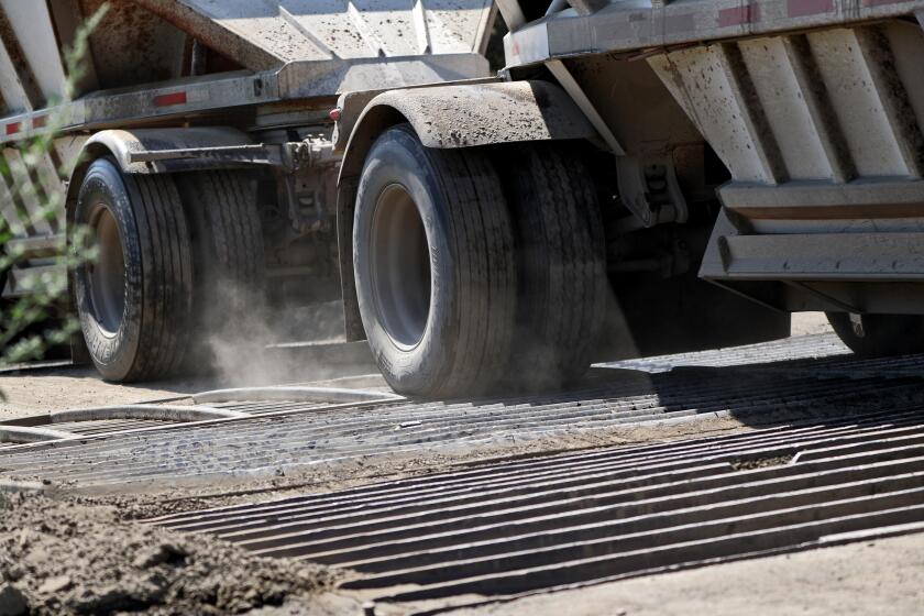 A truck creates dust as it passes over exit metal grates while heading out with a load of dirt from the Hahamongna Watershed Park L.A. County Public Works Department's Devil's Gate Dam Sediment Removal project, in La Canada Flintridge on Tuesday, July 30, 2019.