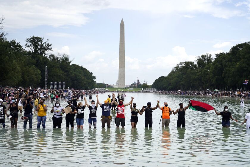 FILE - In this Friday, Aug. 28, 2020, file photo, people join hands as they pose for a photo in the Reflecting Pool in the shadow of the Washington Monument as they attend the March on Washington, at the Lincoln Memorial in Washington, on the 57th anniversary of the Rev. Martin Luther King Jr.'s "I Have A Dream" speech. California lawmakers are setting up a task force to study and make recommendations for reparations to African-Americans, particularly the descendants of slaves, as the nation struggles again with civil rights and unrest following the latest shooting of a Black man by police. The state Senate supported creating the nine-member commission on a bipartisan 33-3 vote Saturday, Aug. 29, 2020. (AP Photo/Julio Cortez, File)