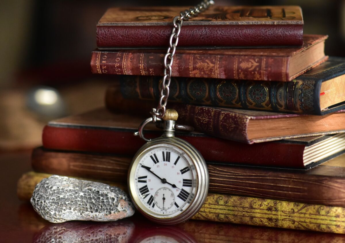 A stack of books sits on a table with a pocket watch draped over them.