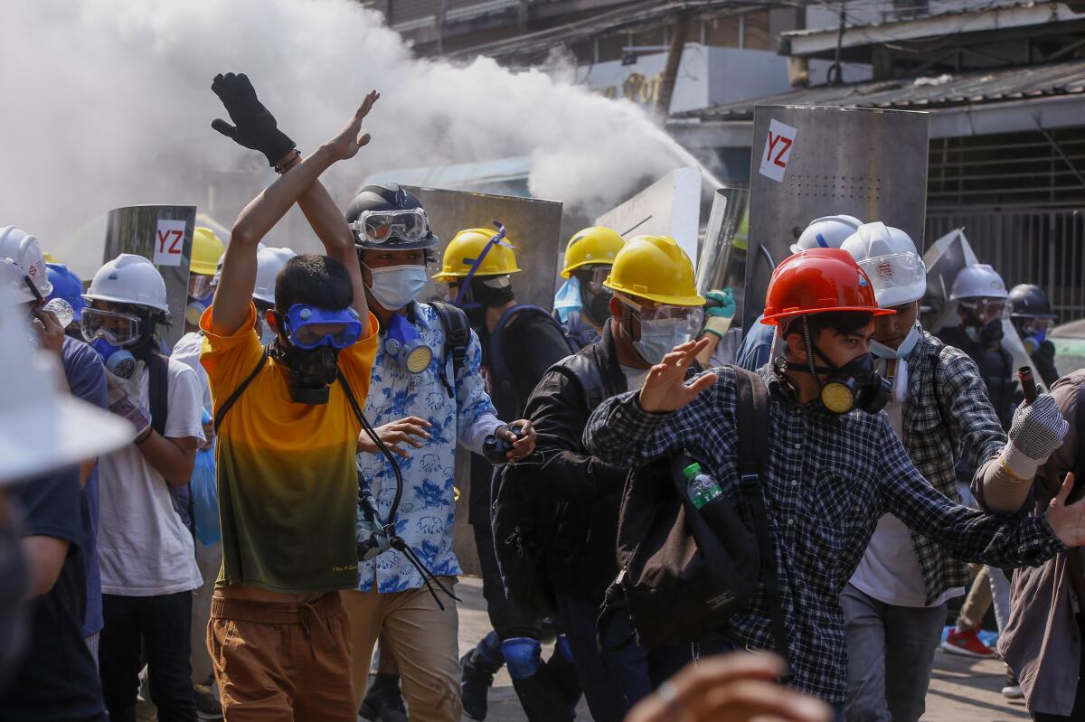 A man crosses his arms overhead as he walks along with others in hard hats, also wearing masks and goggles