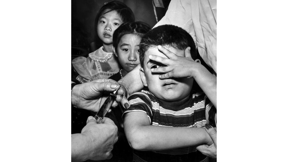 Feb. 25, 1957: Manuel Reyes, 7, peeks apprehensively between fingers at a needle just before getting his polio shot at Castelar Street School as two little girls await their turn.
