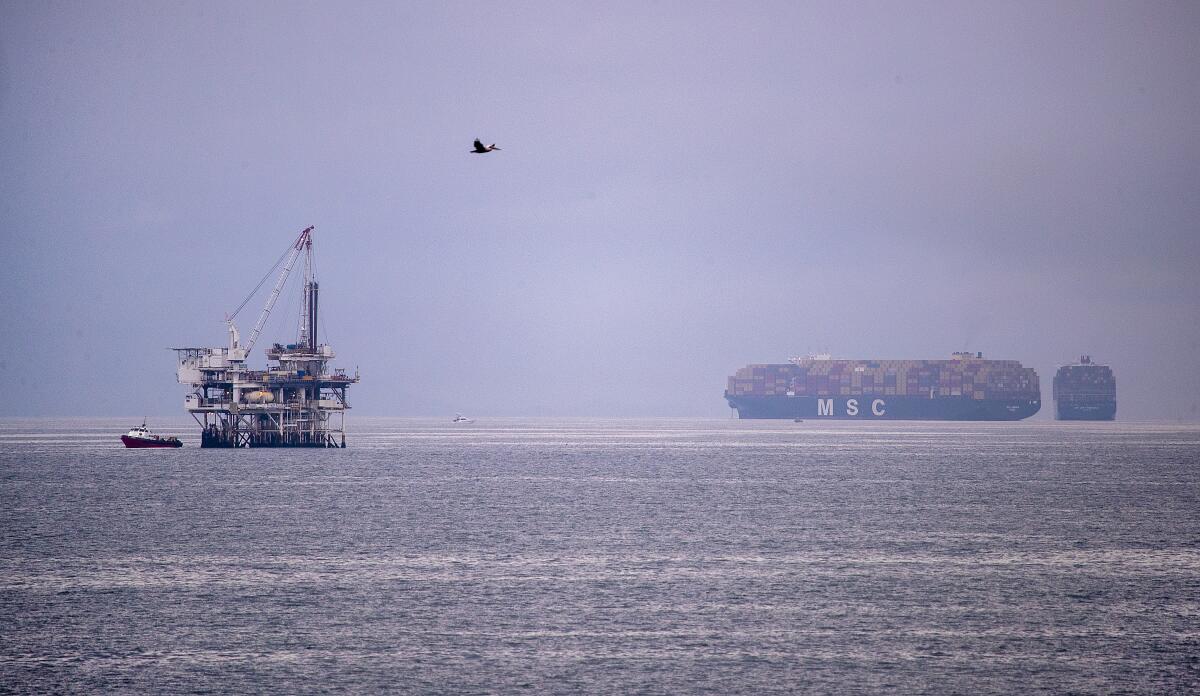 A pelican flies over the Pacific Ocean with a view of an oil rig.