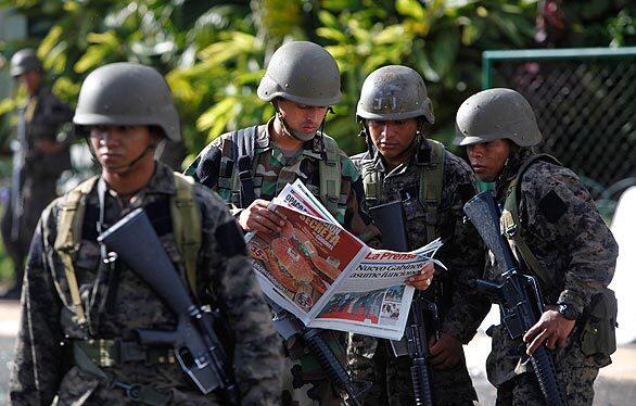 Soldiers read a newspaper outside of the presidential residence in Tegucigalpa, Honduras. The military coup that ousted President Manuel Zelaya on Sunday has sparked clashes in the Honduran capital that have left dozens of people injured.