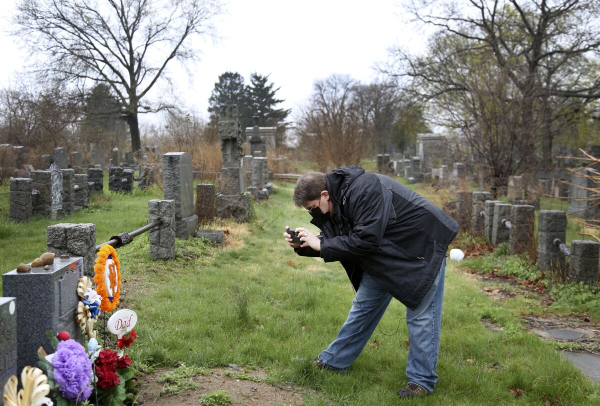 Brian Walter takes a photograph of his late father's gravestone at the All Faiths Cemetery in the Queens borough of New York, Sunday, April 11, 2021. John Walter died from the coronavirus May 10, 2020. (AP Photo/Jessie Wardarski)