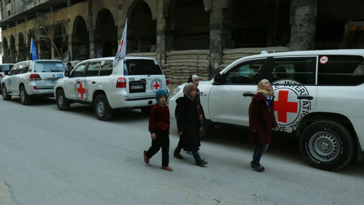 Syrian children walk past vehicles of the U.N. and the International Committee of the Red Cross delivering humanitarian aid in the Syrian town of Duma on the eastern outskirts of the capital, Damascus, on Friday.