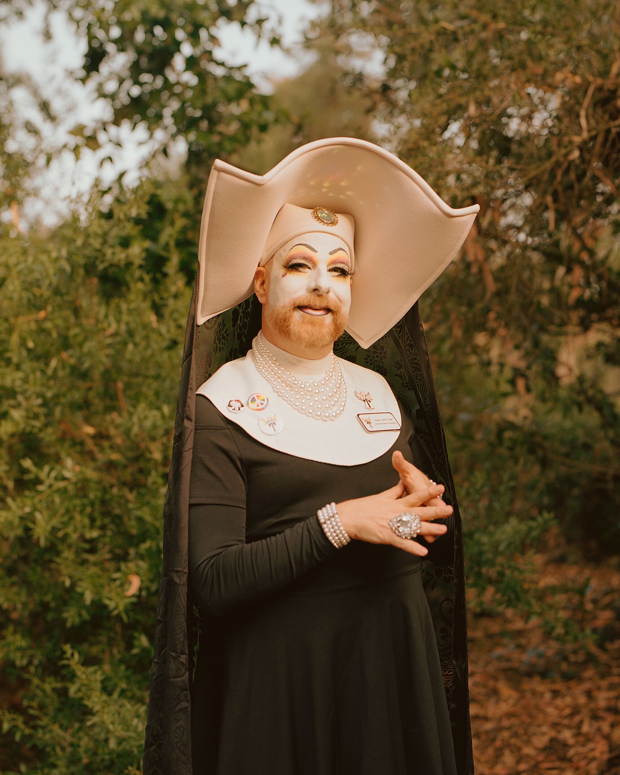 A drag nun with white fact paint stands outdoors
